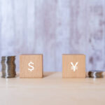 Wooden blocks with a Japanese yen sign and a dollar sign, and coins.
