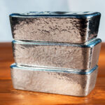 Three cast silver bullion on a mahogany background